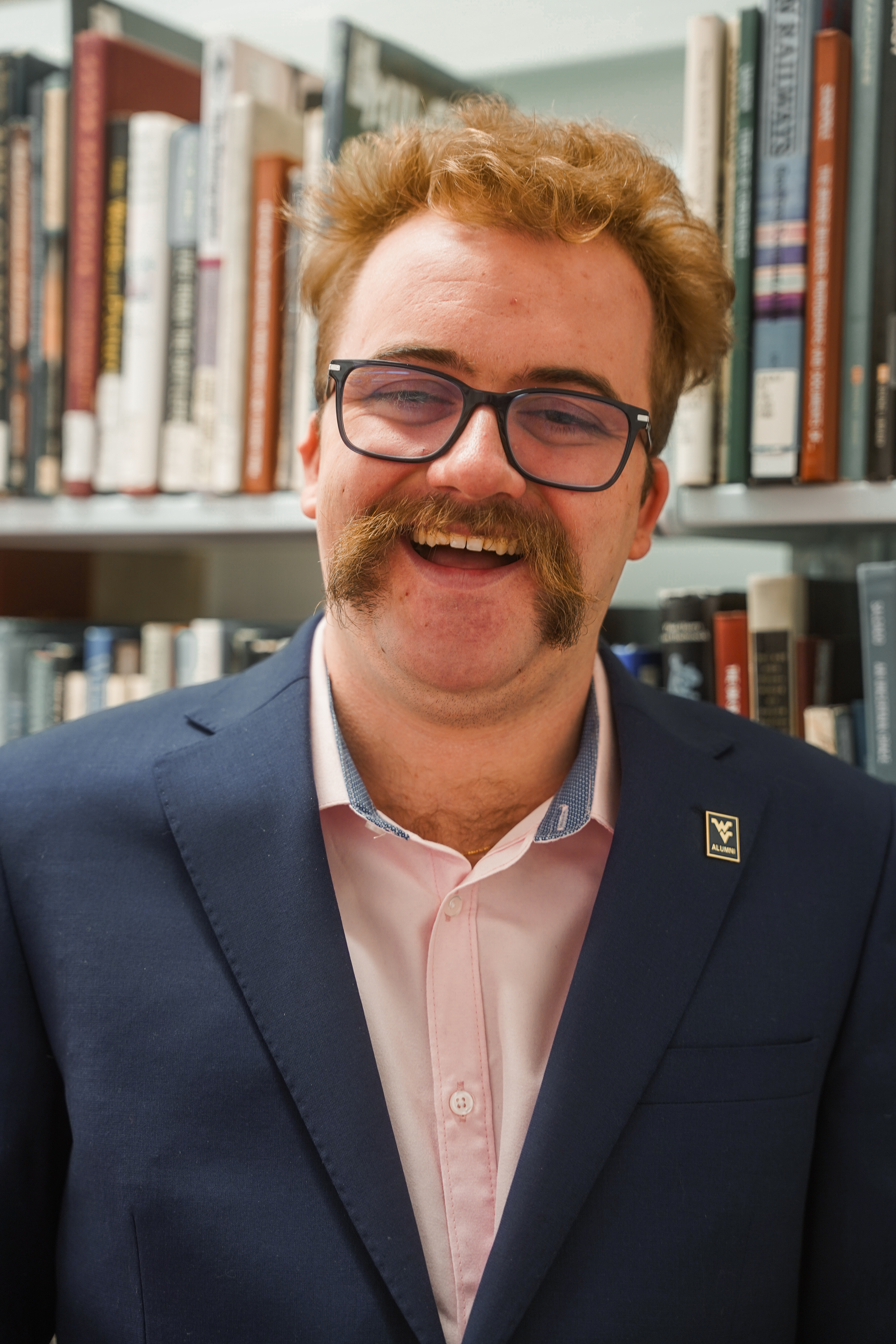 Tannor Enyart smiling in a navy jacket in front of library shelves